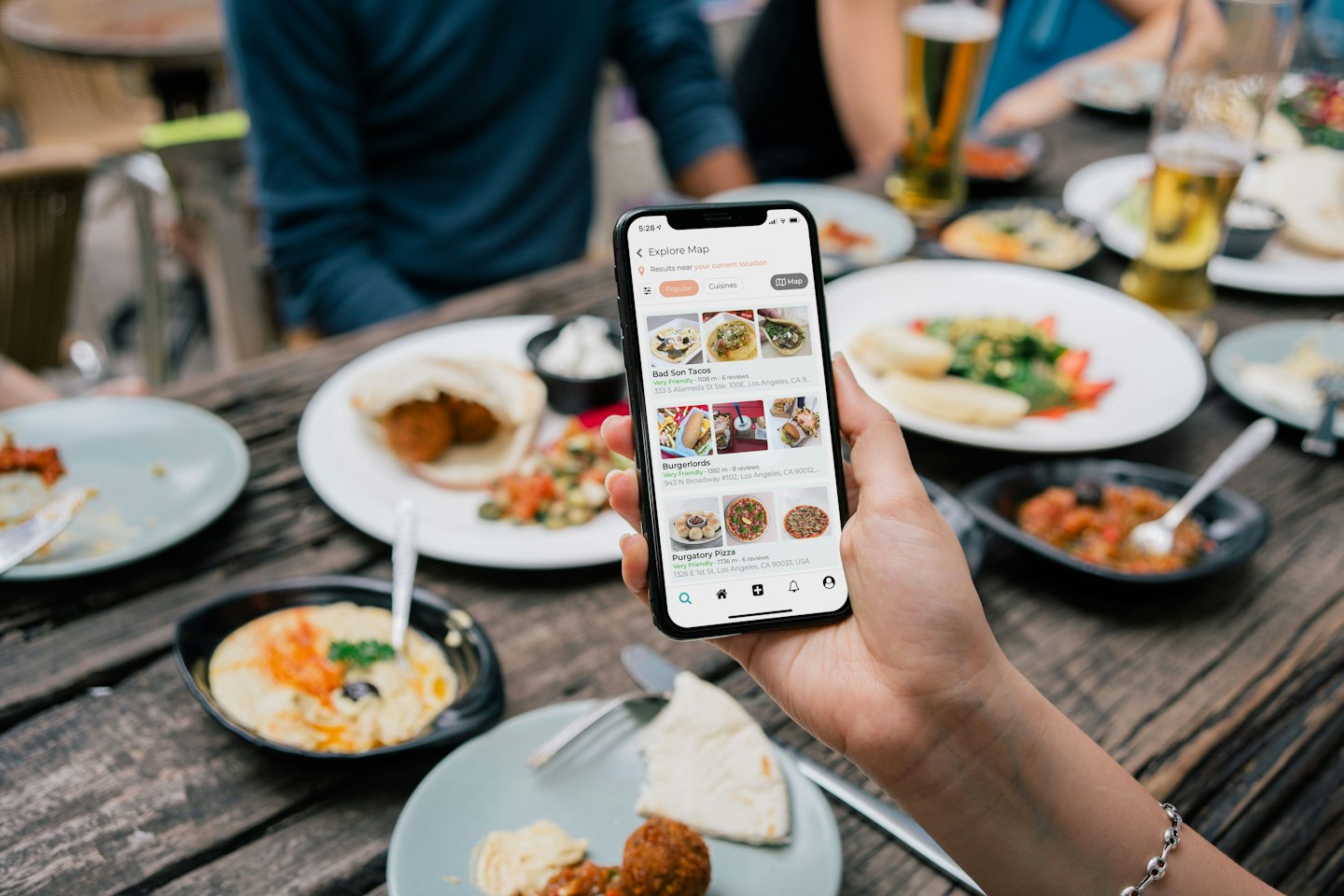 Hand holding phone with food app at table with dishes.